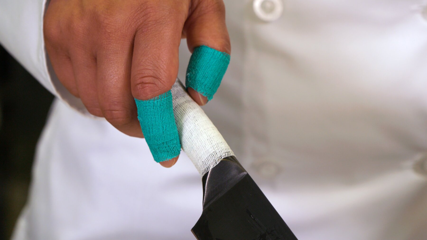 Chef with tape-wrapped fingers holding knife with wrapped handle